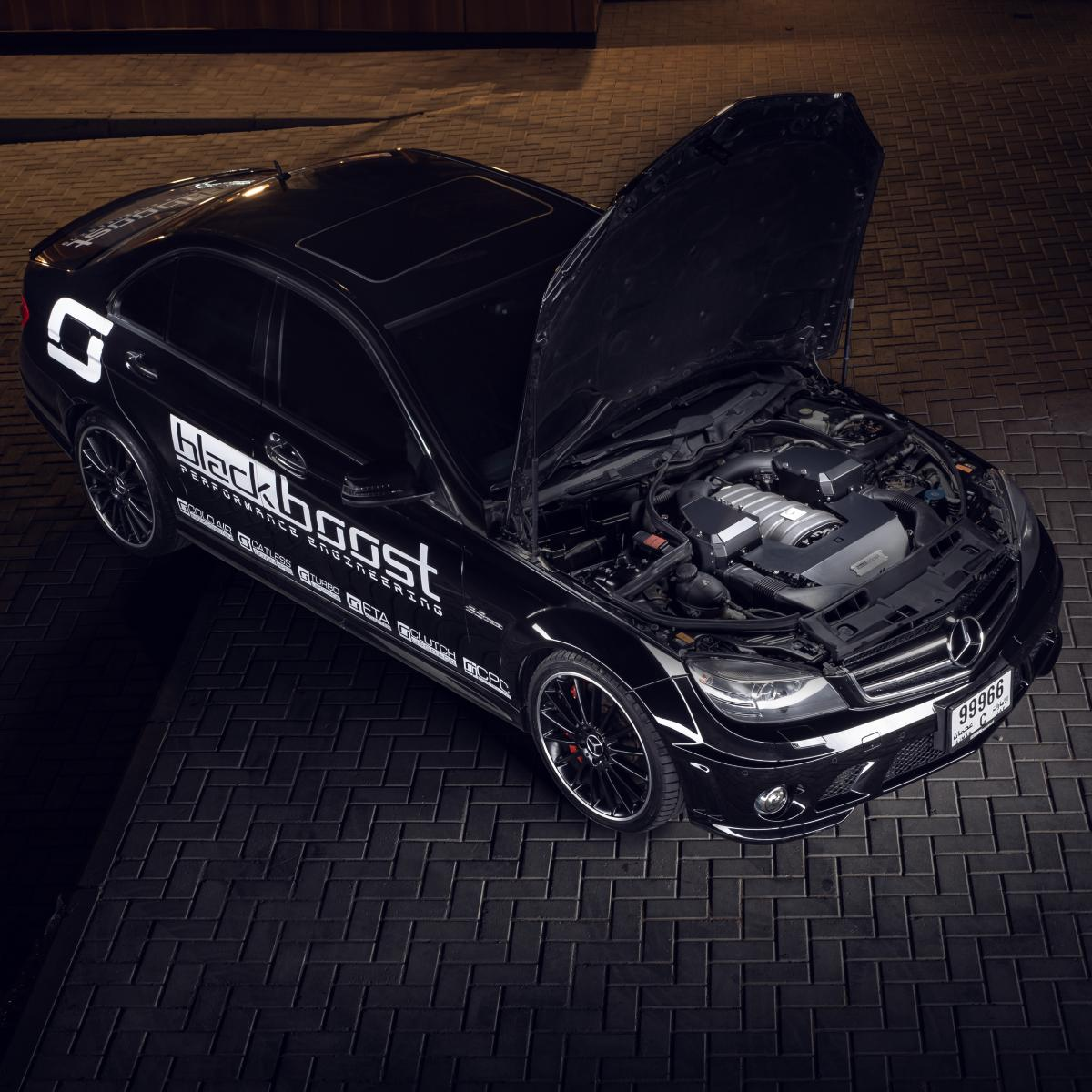 Overhead view of a black Mercedes-Benz performance sedan with hood open, showcasing a modified engine bay and Blackboost performance branding.