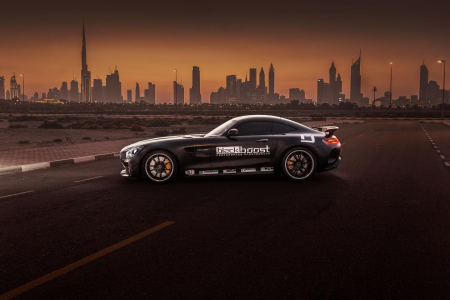 Black matte Mercedes-AMG sports car with performance decals parked on an empty road at sunset, Dubai skyline and Burj Khalifa in the background